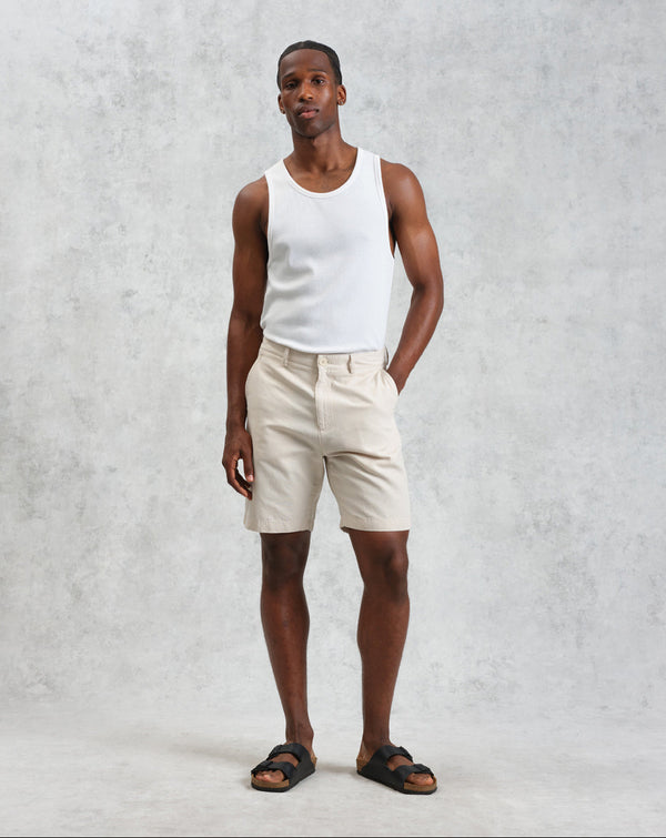 Man wearing a white tank top and beige shorts against a gray background