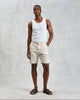 Man wearing a white tank top and beige shorts against a gray background